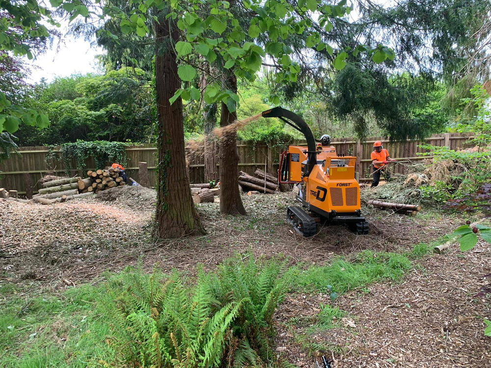 A tracked chipper working in a large garden with logs stacked behind